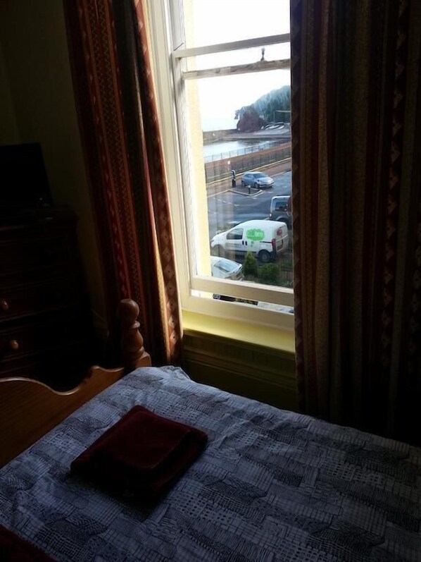 Una habitación con cama, ventana y vistas a una calle con coches y un edificio.