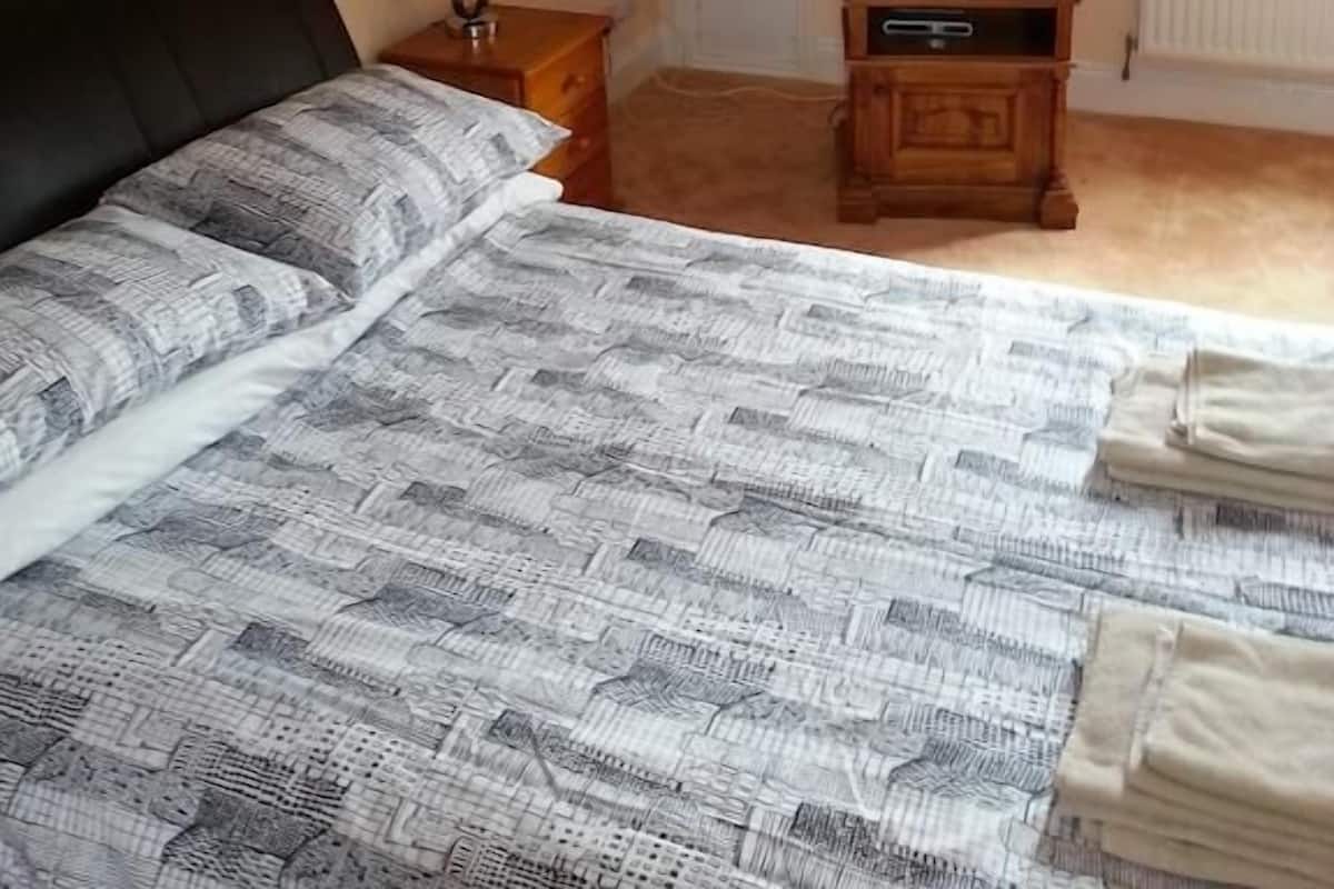 A bedroom with a bed, a television on a wooden stand, a lamp, and a radiator.