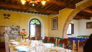 Un comedor con una mesa larga dispuesta para una comida, vigas de madera en el techo y una mesa de billar al fondo.
