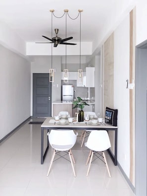 Un comedor moderno con una mesa oscura, sillas blancas, lámparas colgantes y un ventilador de techo.