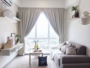 Un salon moderne avec une grande fenêtre, un canapé gris et une petite table agrémentée d’objets décoratifs.
