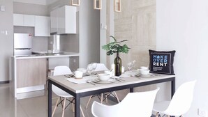A modern kitchen with white cabinets, a refrigerator, and a dining area with a table set for two. - Gombak126 HomeStay (Kuala Lumpur)