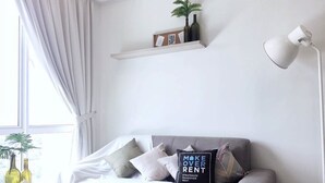 A modern living room with a grey sofa, a white coffee table, and a side table. There are two potted plants, a white floor lamp, and a shelf with decorative items. - Gombak126 HomeStay (Kuala Lumpur)
