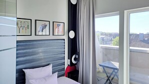 Una habitación de hotel con una cama, cabecera, ventana con cortinas y balcón.