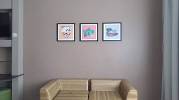 A room with a beige sofa, a green ottoman, and three framed artworks on the wall.