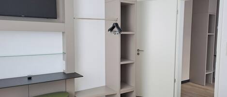 Ein modernes Schlafzimmer mit Bett, einem grünen Hocker, einem an der Wand montierten Fernseher und einem Kleiderschrank mit Ablagefläche.