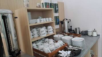 A kitchen area with shelves stocked with white mugs, plates, and a coffee machine.