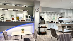 Un café moderno con mostrador, zona de estar y cocina al fondo.