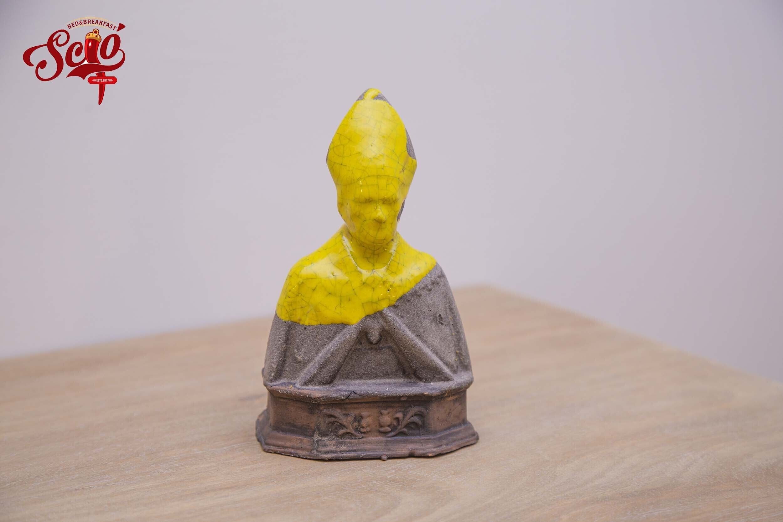 Una piccola statua con la parte superiore gialla e la base marrone, posata su una superficie di legno.