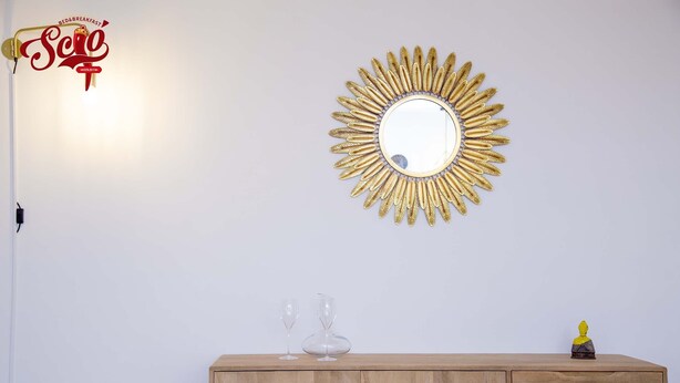 A room with a wooden cabinet, a mirror with a sunburst frame, and a bed with a headboard.