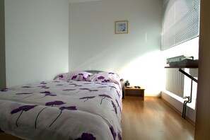 Un dormitorio con cama, mesita de noche, un cuadro en la pared y ventana con persianas.