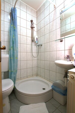 Un baño pequeño con inodoro, ducha con cortina, lavamanos y espejo.