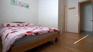 A bedroom with a wooden bed, white walls, and a door leading to another room. - Guesthouse Ivac Inn Zagreb Airport (Velika Gorica)