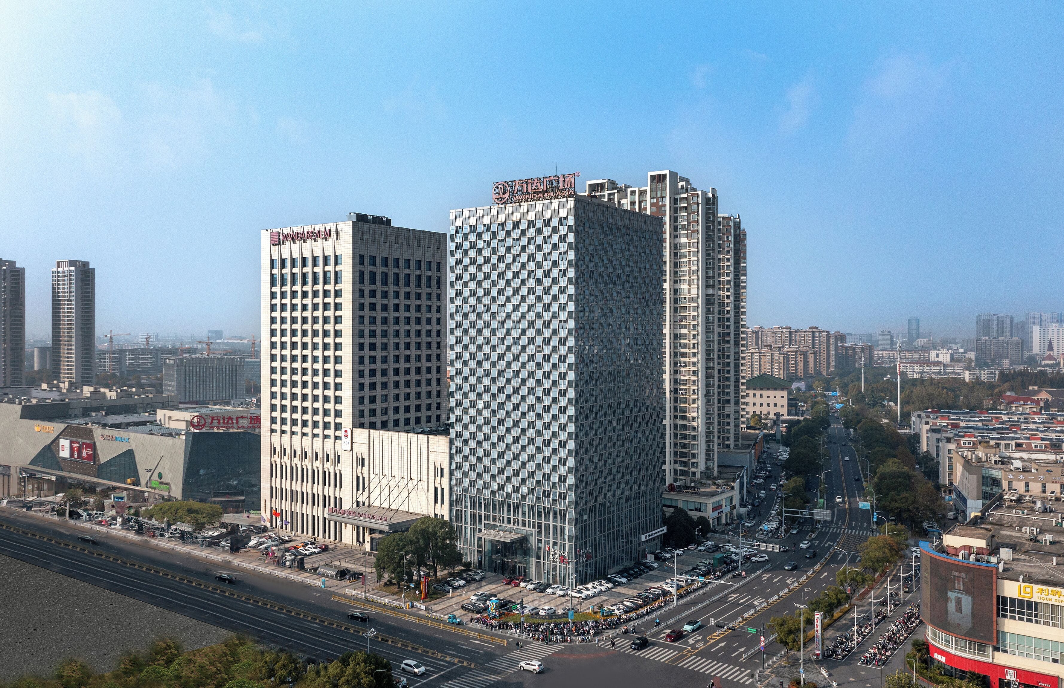 Paisagem urbana com edifícios modernos altos, um cruzamento movimentado e céu claro.