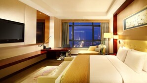 A hotel room with a large bed, a desk, a TV, and a view of the city at night. - Wanda Realm Taizhou (Taizhou)