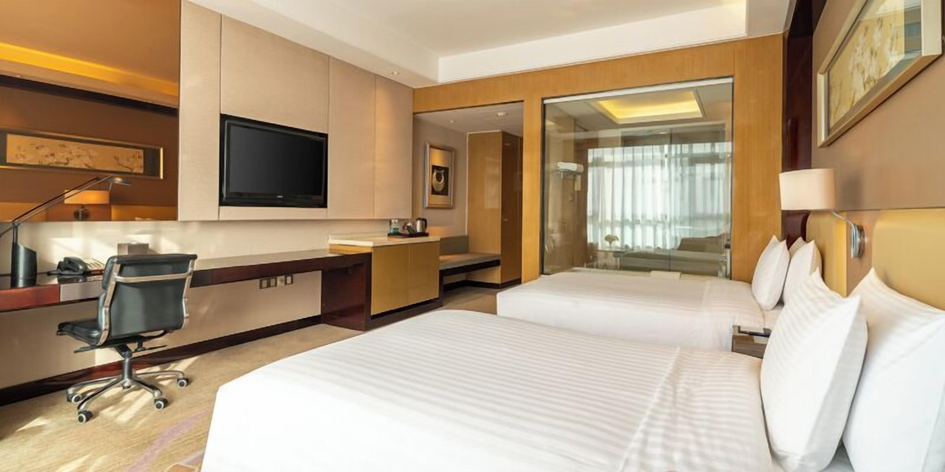 Ein Hotelzimmer mit einem Bett, einem Schreibtisch, einem Sessel, einem Fernseher und einem großen Fenster.