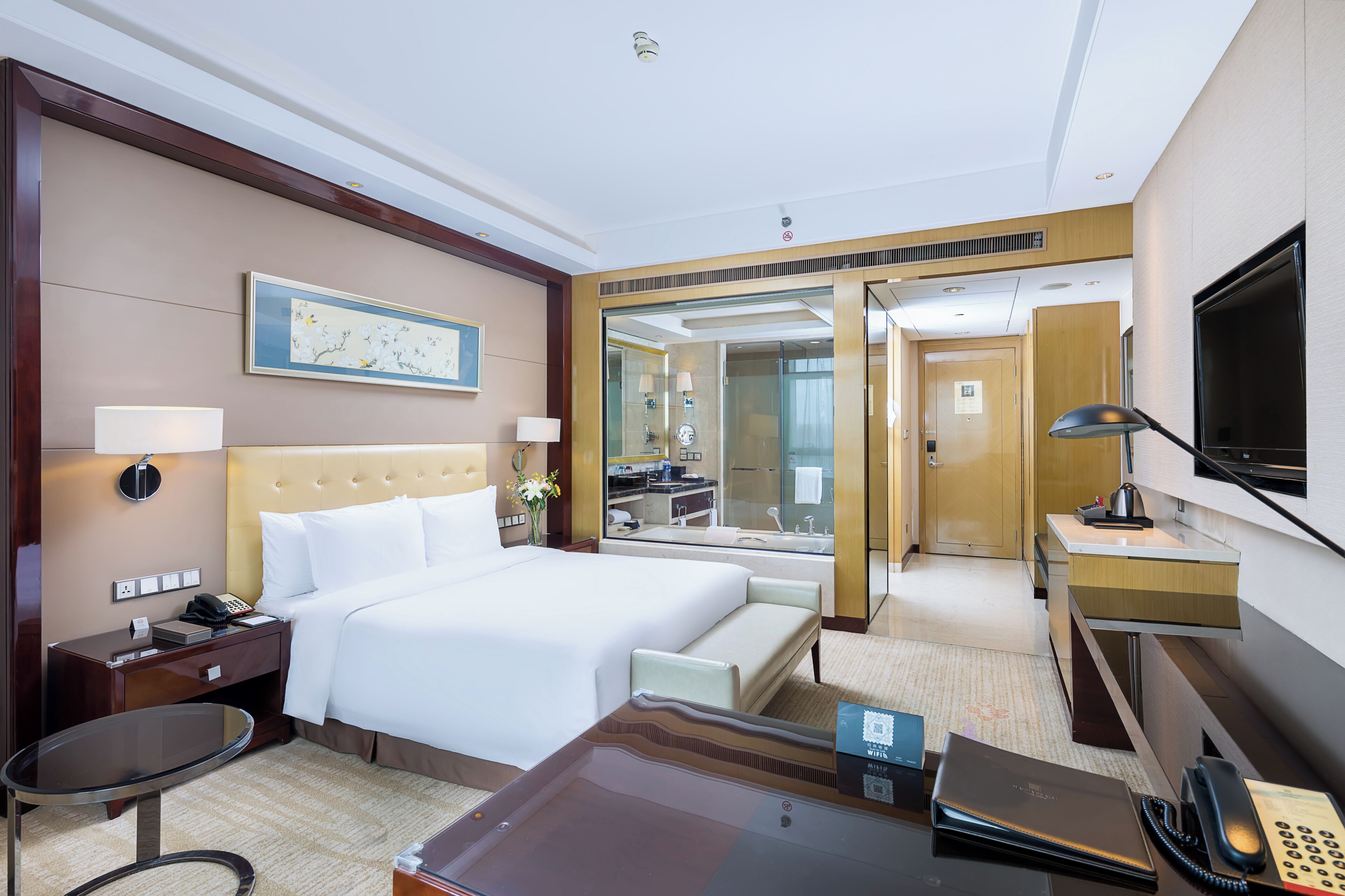 Una habitación de hotel con una cama grande, un escritorio con ordenador, un espejo y un televisor.