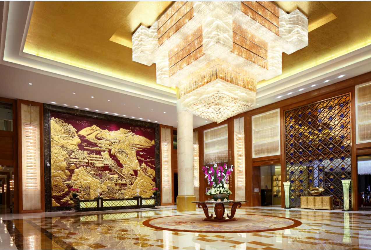 A spacious lobby with a large golden mural, a central round table, and a decorative chandelier.