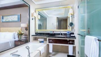 Un baño de hotel moderno con un espejo grande, una bañera, una ducha y un tocador con lavabo.