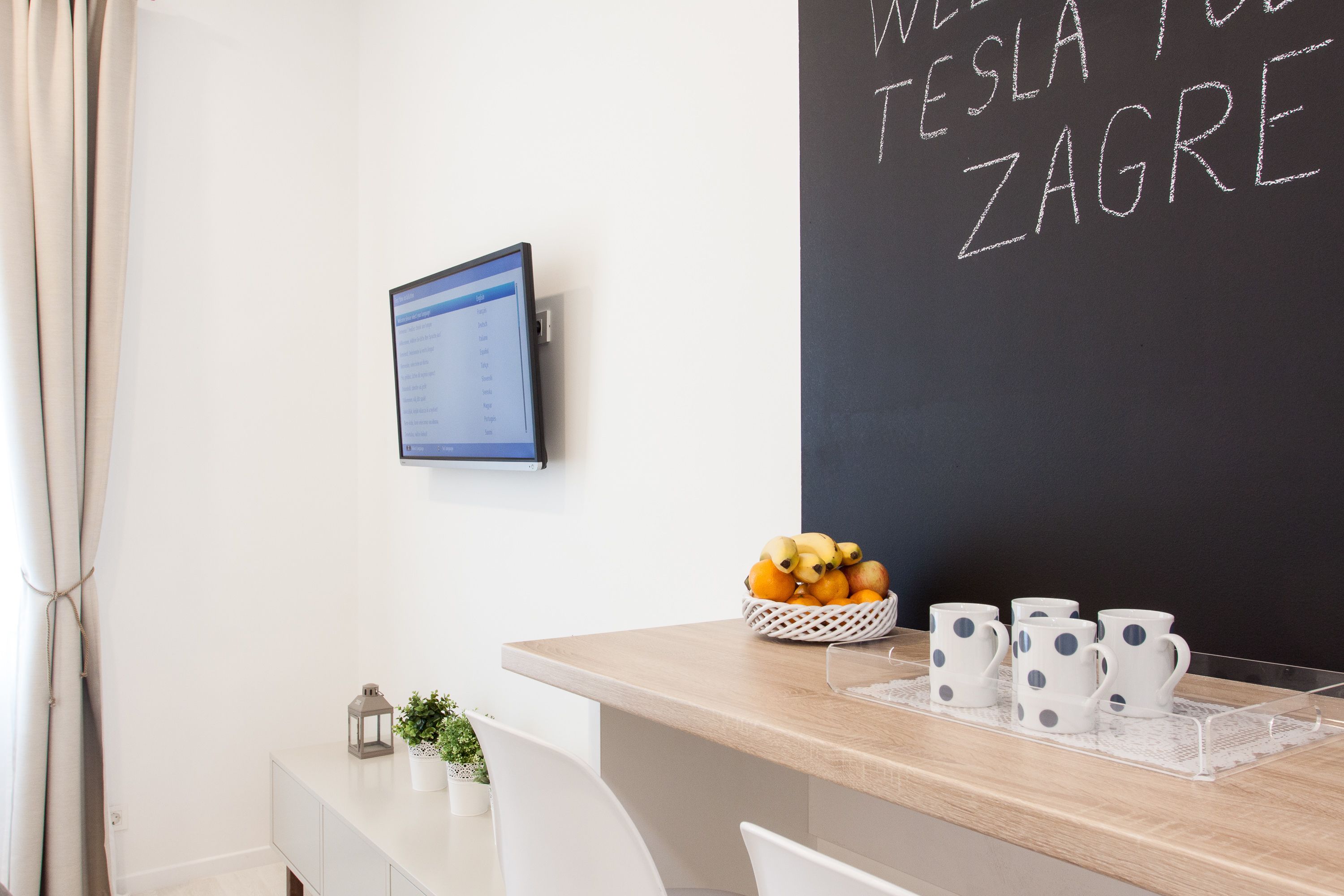 Une pièce moderne équipée d’un bureau, d’un écran d’ordinateur, d’un tableau noir avec du texte, d’un panier de fruits et de tasses à pois.