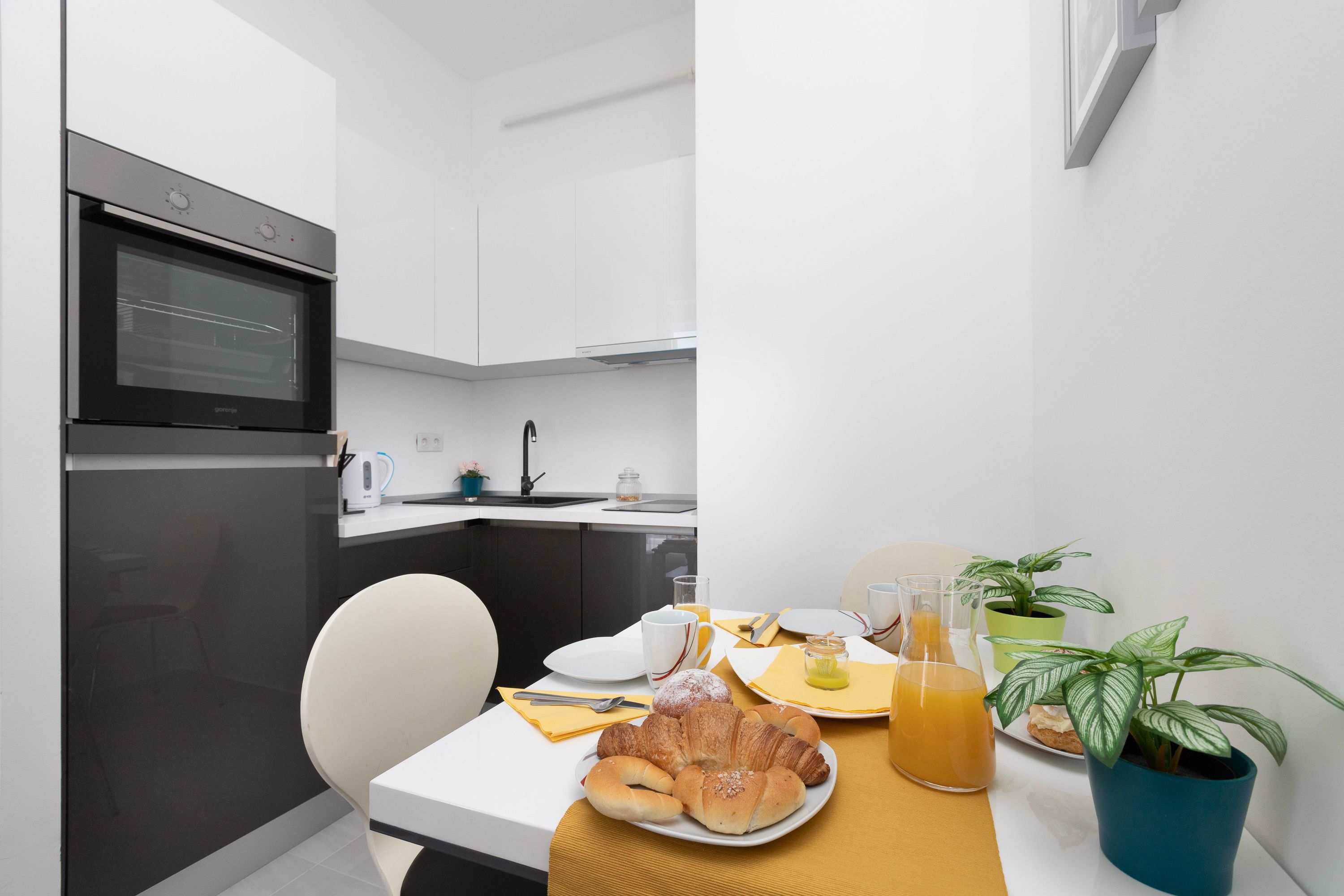 Una cocina moderna con una mesa lista para el desayuno, que incluye cruasanes y jugo de naranja.