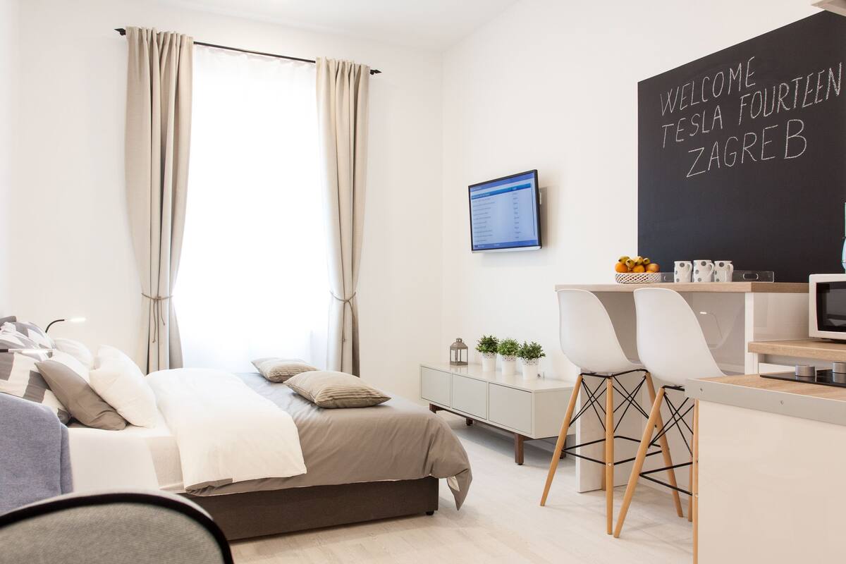 Une chambre d’hôtel moderne équipée d’un lit, d’un bureau avec un ordinateur et d’un tableau noir sur lequel est écrit un message de bienvenue.