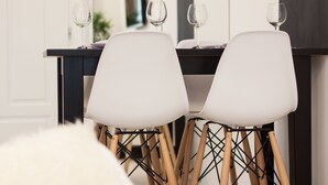 Een eethoek met twee witte stoelen op houten poten, een donkere tafel en twee wijnglazen.