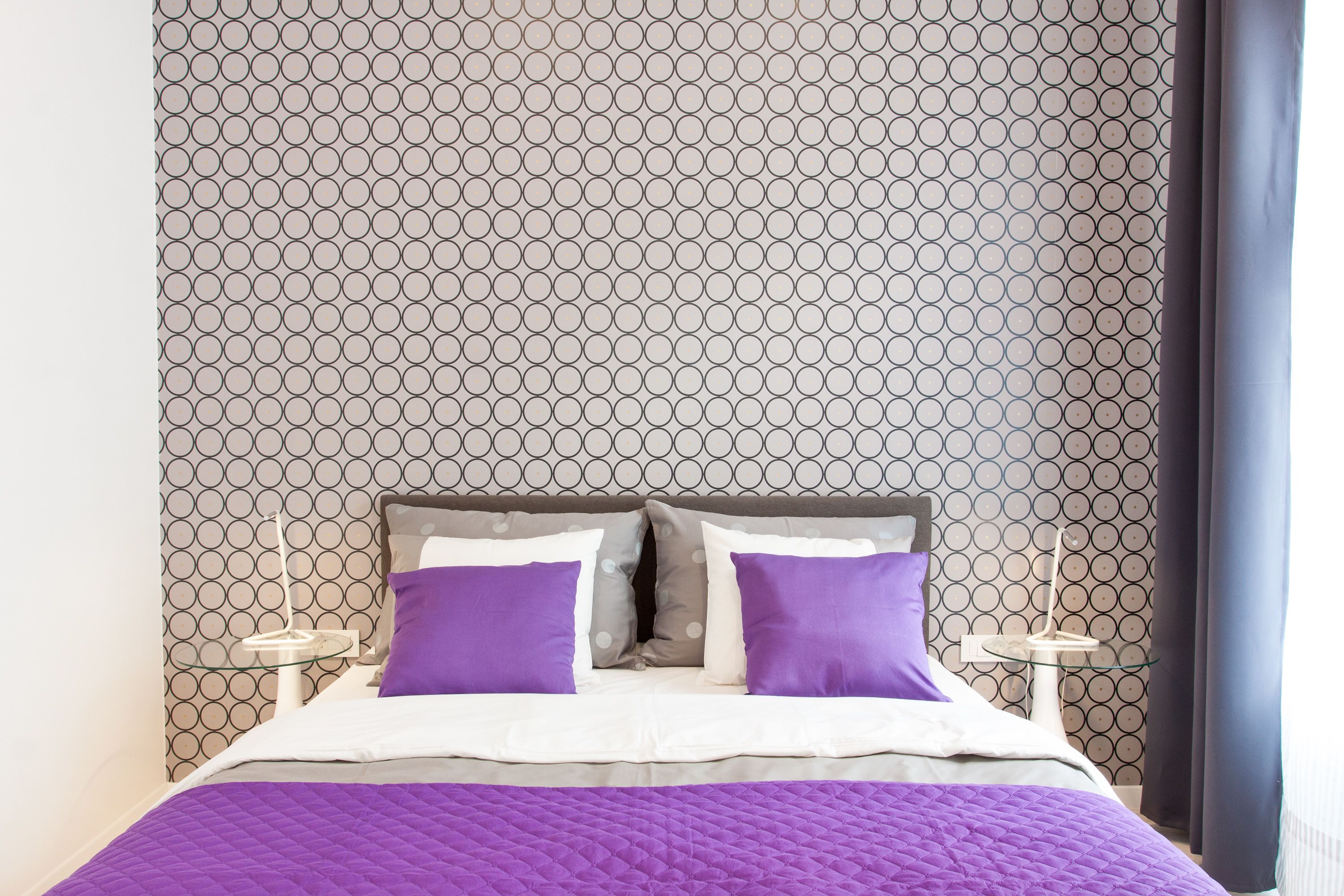 A neatly made bed with a patterned headboard, two pillows, and a purple blanket.