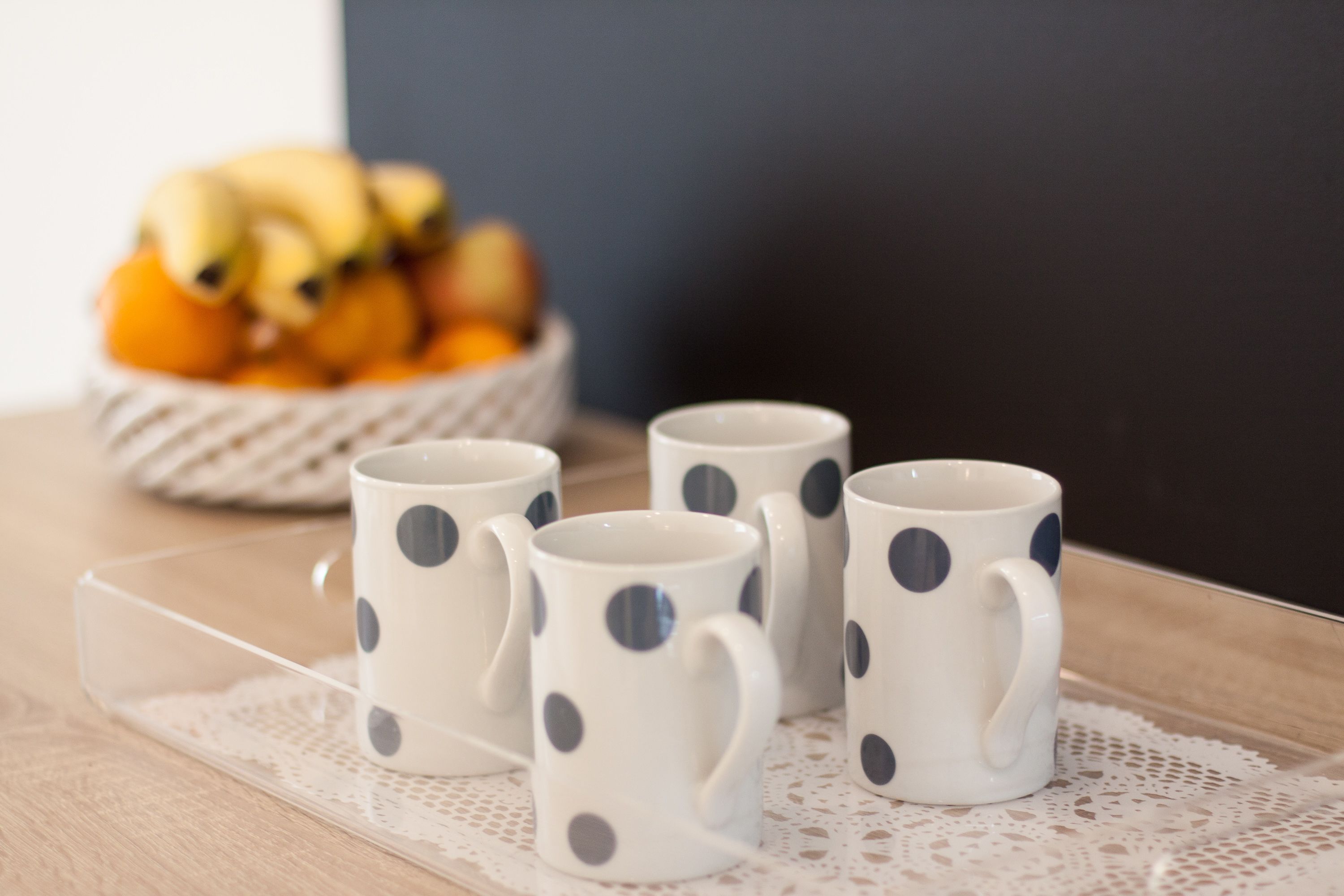 Quatre tasses blanches à pois bleu foncé, disposées sur un plateau transparent.