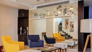 Una sala de estar moderna con sillas amarillas y azules, una mesa de centro y una escalera al fondo.