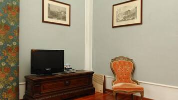 Una habitación con una televisión sobre un mueble de madera, una silla antigua y dos fotografías en blanco y negro enmarcadas en la pared.