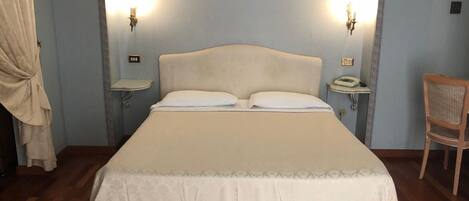 A neatly made bed with a headboard, two bedside lamps, a bedside telephone, and a wooden chair.