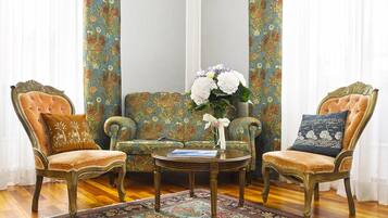 Una habitación con dos sillas ornamentadas, una mesita pequeña y un sofá estampado con motivos florales.