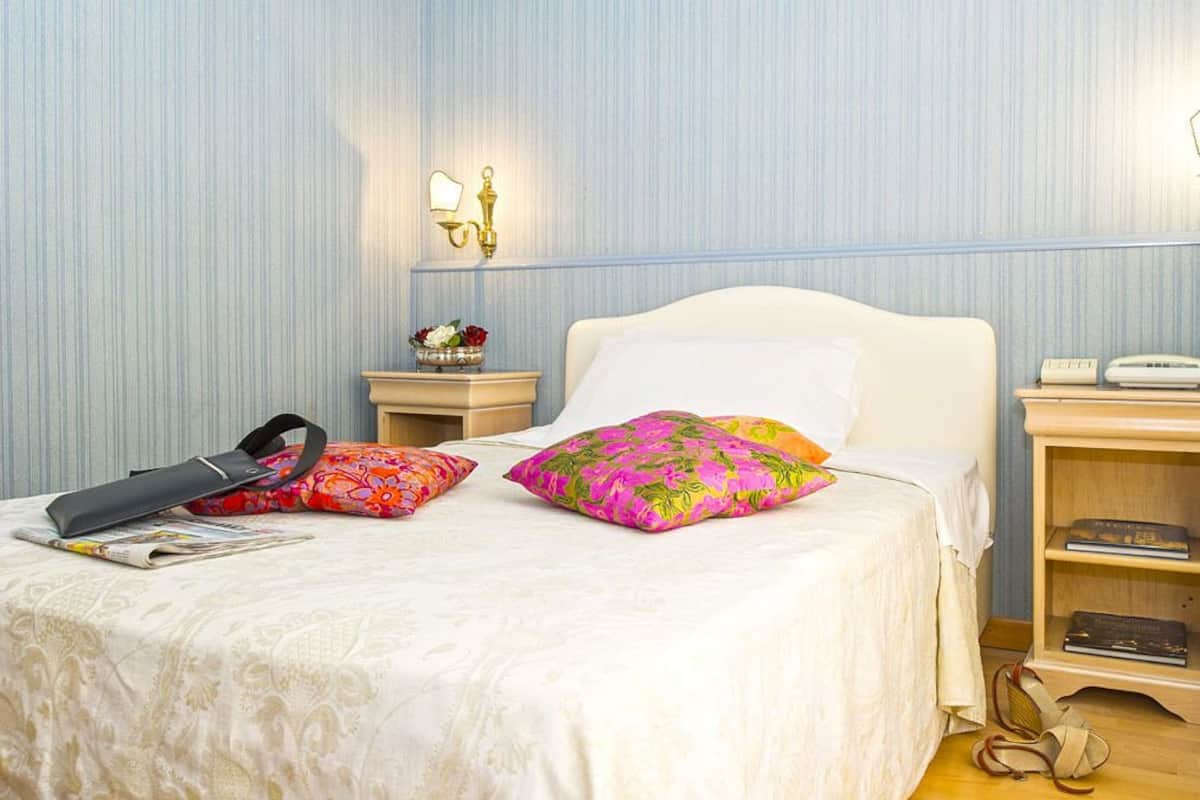 A neatly made bed with a white headboard, a bedside table with a lamp, and a small shelf with books.