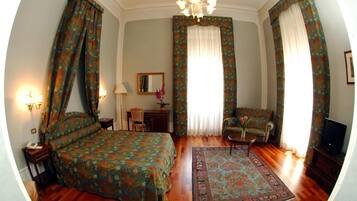 A bedroom with a bed, a desk, a chair, a television, and a chandelier.
