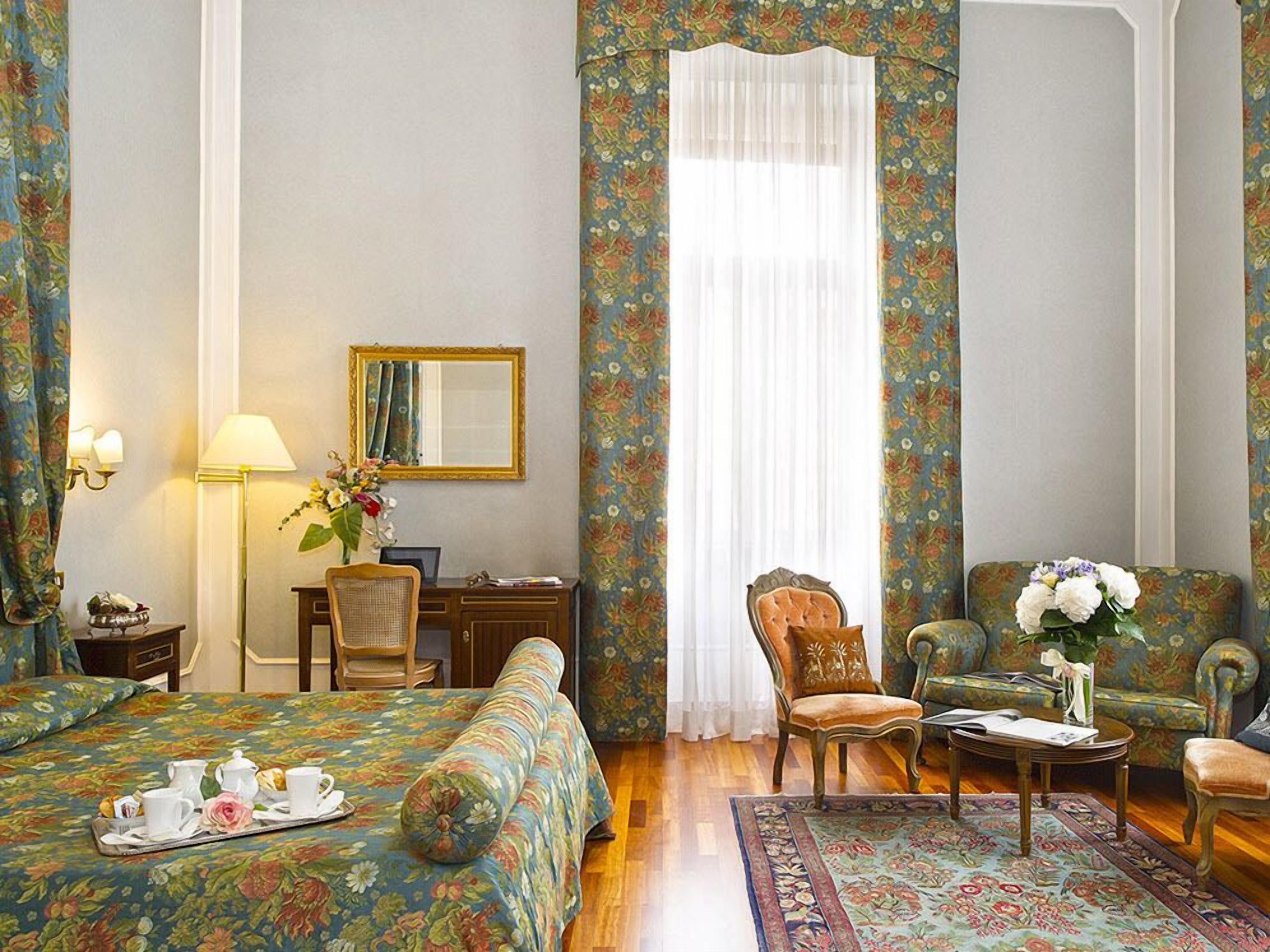 Une chambre d’hôtel avec un lit, deux chaises, un bureau, une lampe et un miroir.