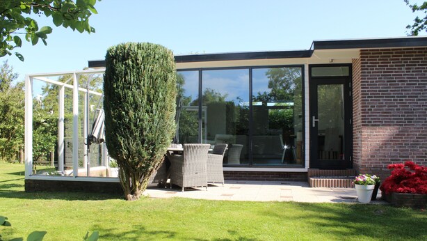 Ein modernes Haus mit Wintergarten, Terrasse und Gartenmöbeln sowie einem gepflegten Rasen.
