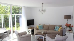 Ein Wohnzimmer mit einer Couch, zwei Sesseln, einem Couchtisch, einem Fernseher und einer Deckenleuchte.