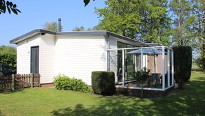 Ein eingeschossiges Haus mit einer verglasten Veranda, einem kleinen eingezäunten Garten und einem Schornstein.