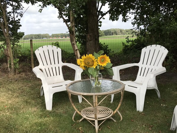 Dos sillas blancas de plástico, una mesa redonda de vidrio y un jarrón con girasoles.