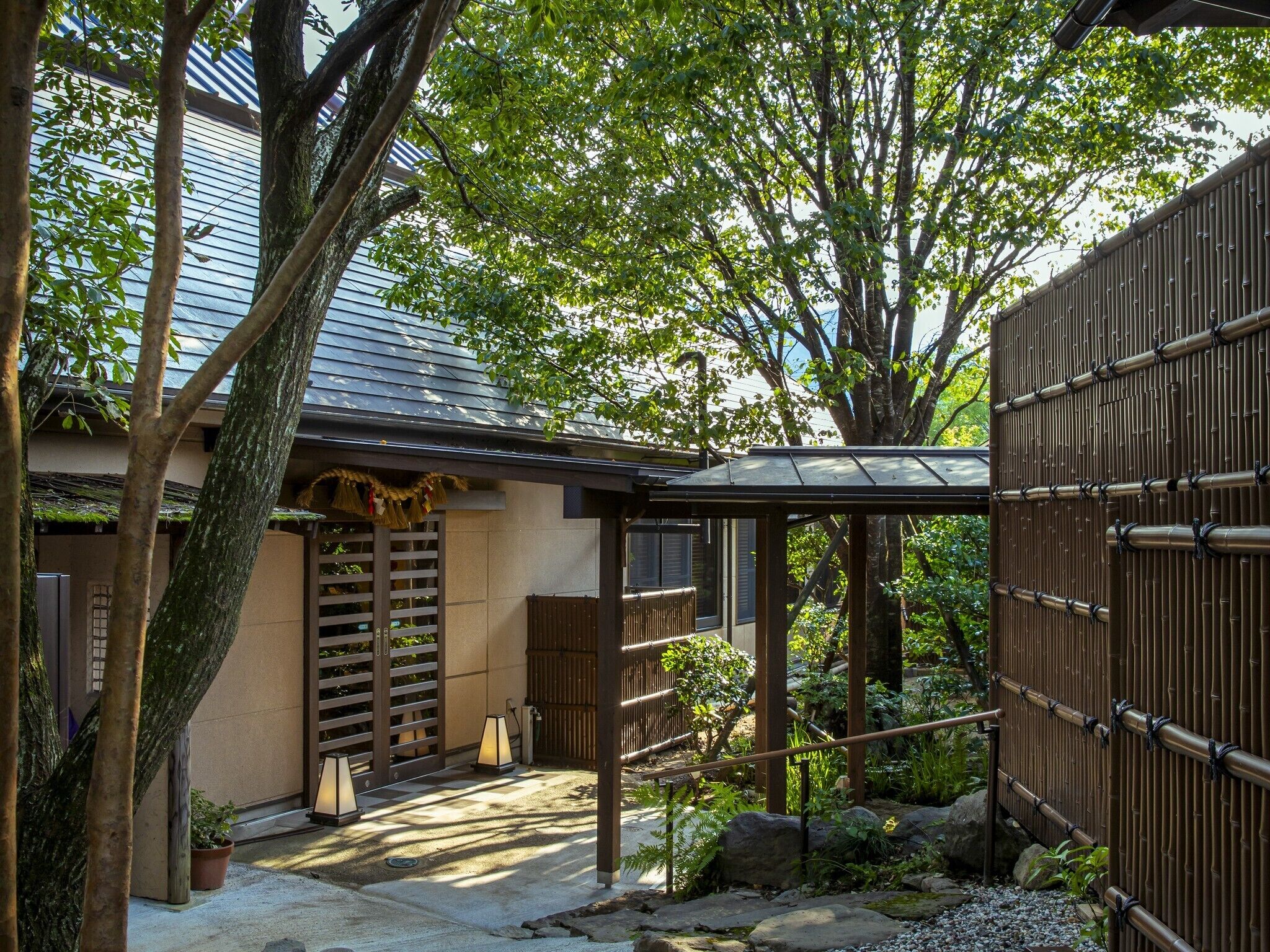 Un jardín japonés tradicional con una casa de madera, una cerca de bambú y un sendero de piedra.