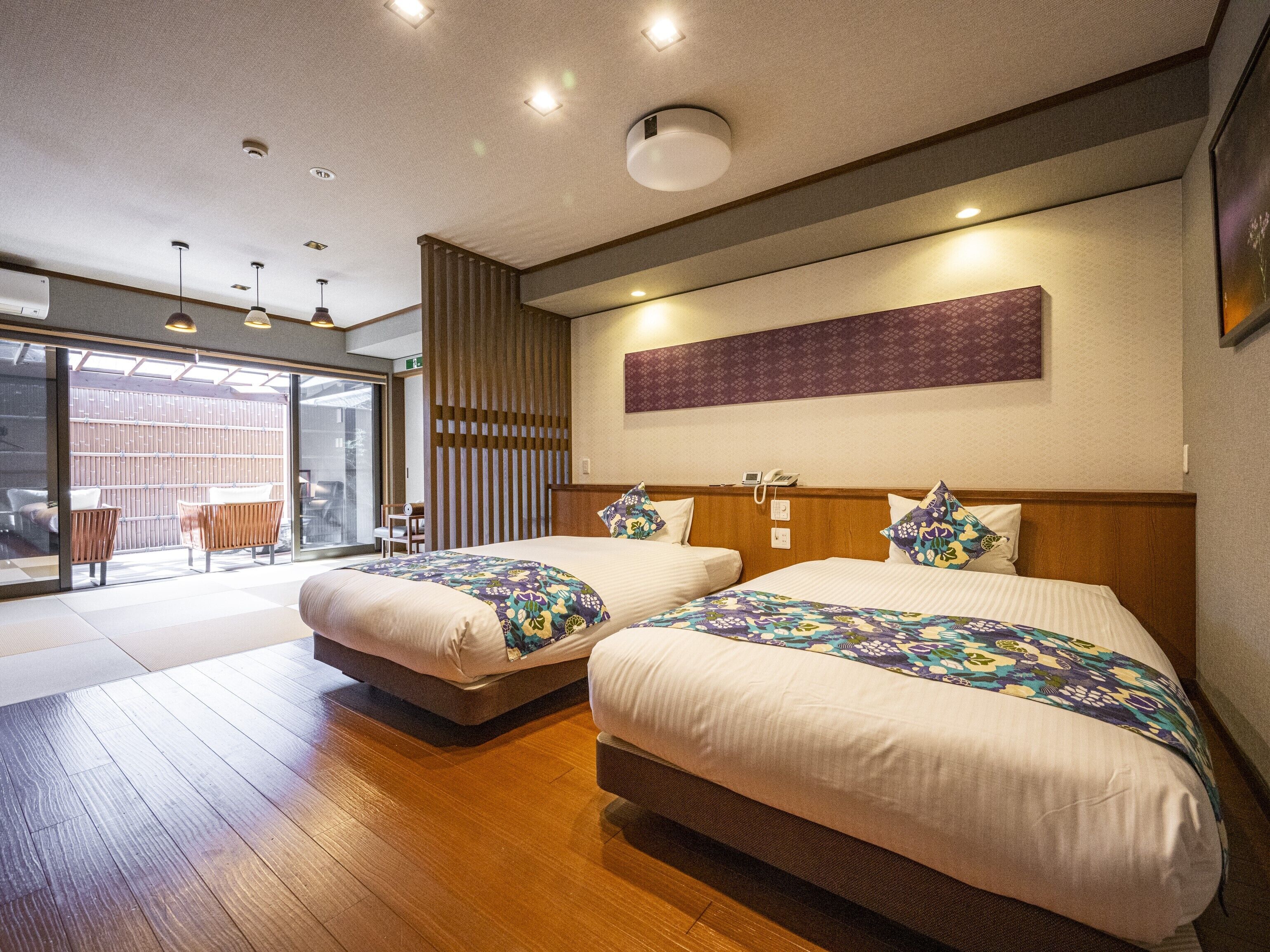 Una habitación de hotel moderna con dos camas, un ventanal grande y un cerramiento de vidrio corredero que da a un espacio exterior.