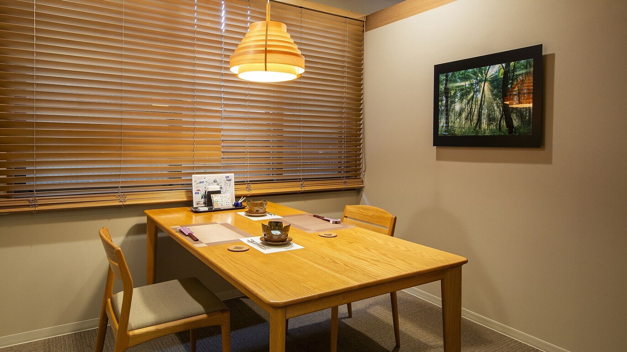 Un comedor con una mesa de madera, sillas, una lámpara colgante, un cuadro en la pared y una ventana con persianas.