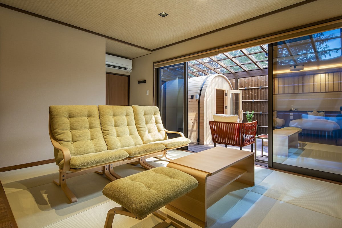 Ein modernes Interieur mit Sofa und Bank, einem kleinen Tisch und Blick durch eine Glastür auf ein Schlafzimmer.