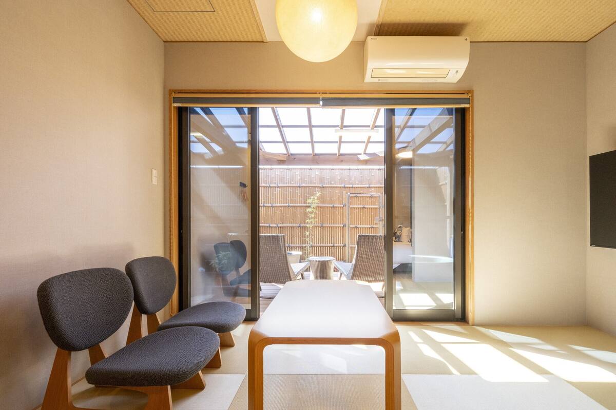 Ein Zimmer mit Tatami-Boden, einem niedrigen Holztisch und vier dunklen Stühlen.