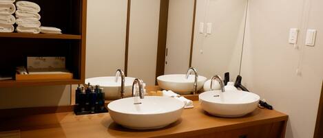 A bathroom with two sinks, a mirror, a fan, and a shelf with towels.
