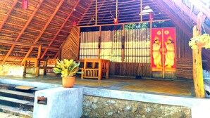 A traditional wooden structure with a thatched roof, a stone wall, and a wooden bench. - Habarana Ambasewana Resort (Habarana)