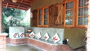 A covered outdoor seating area with a bench and cushions, a brick wall, and wooden windows. - Habarana Ambasewana Resort (Habarana)