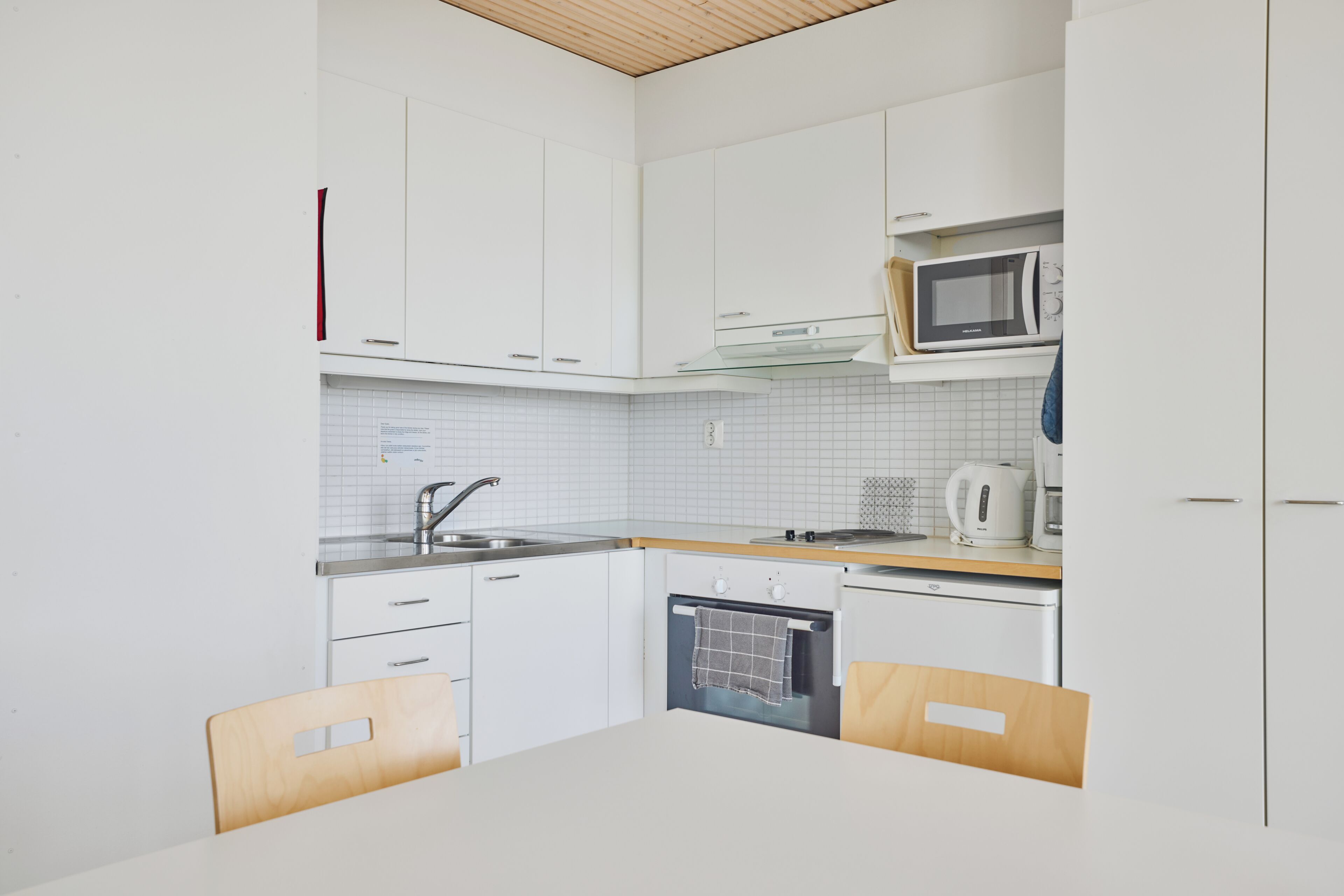 A compact kitchen with white cabinets, a microwave, a kettle, and a dishwasher.