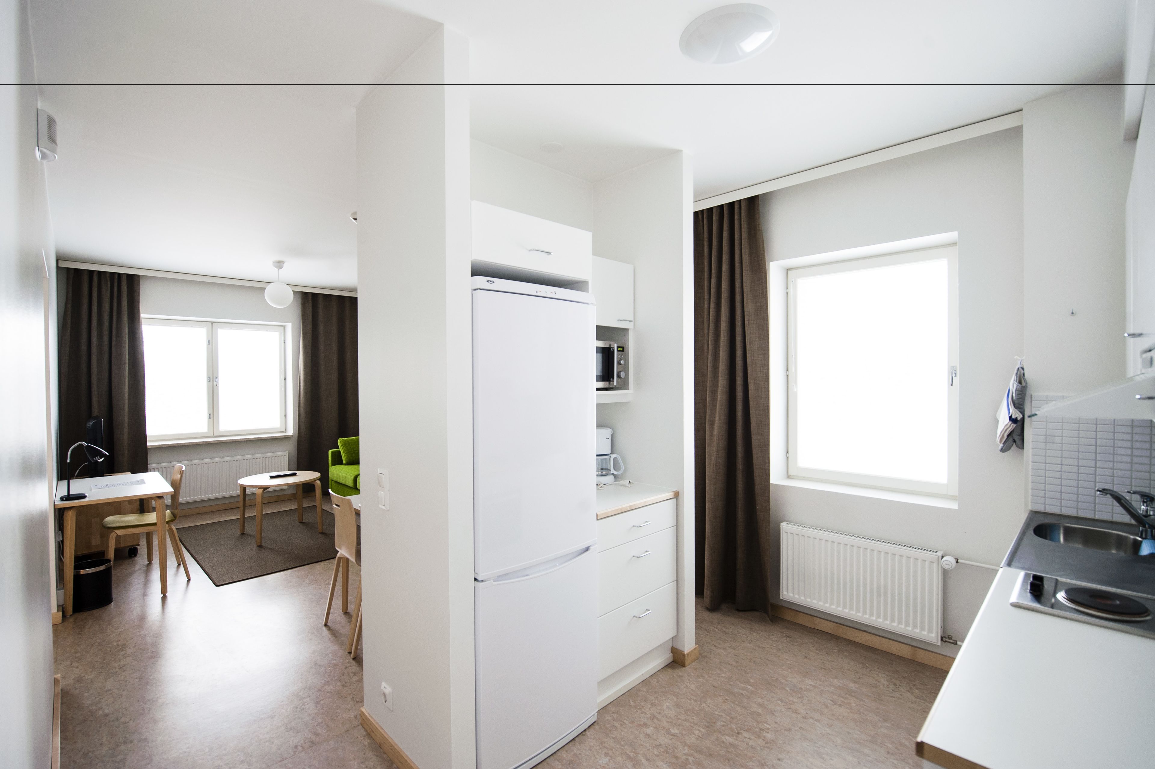 Et moderne køkken med hvide hårde hvidevarer, et spiseområde med bord og stole, samt et stort vindue der giver naturligt lys.